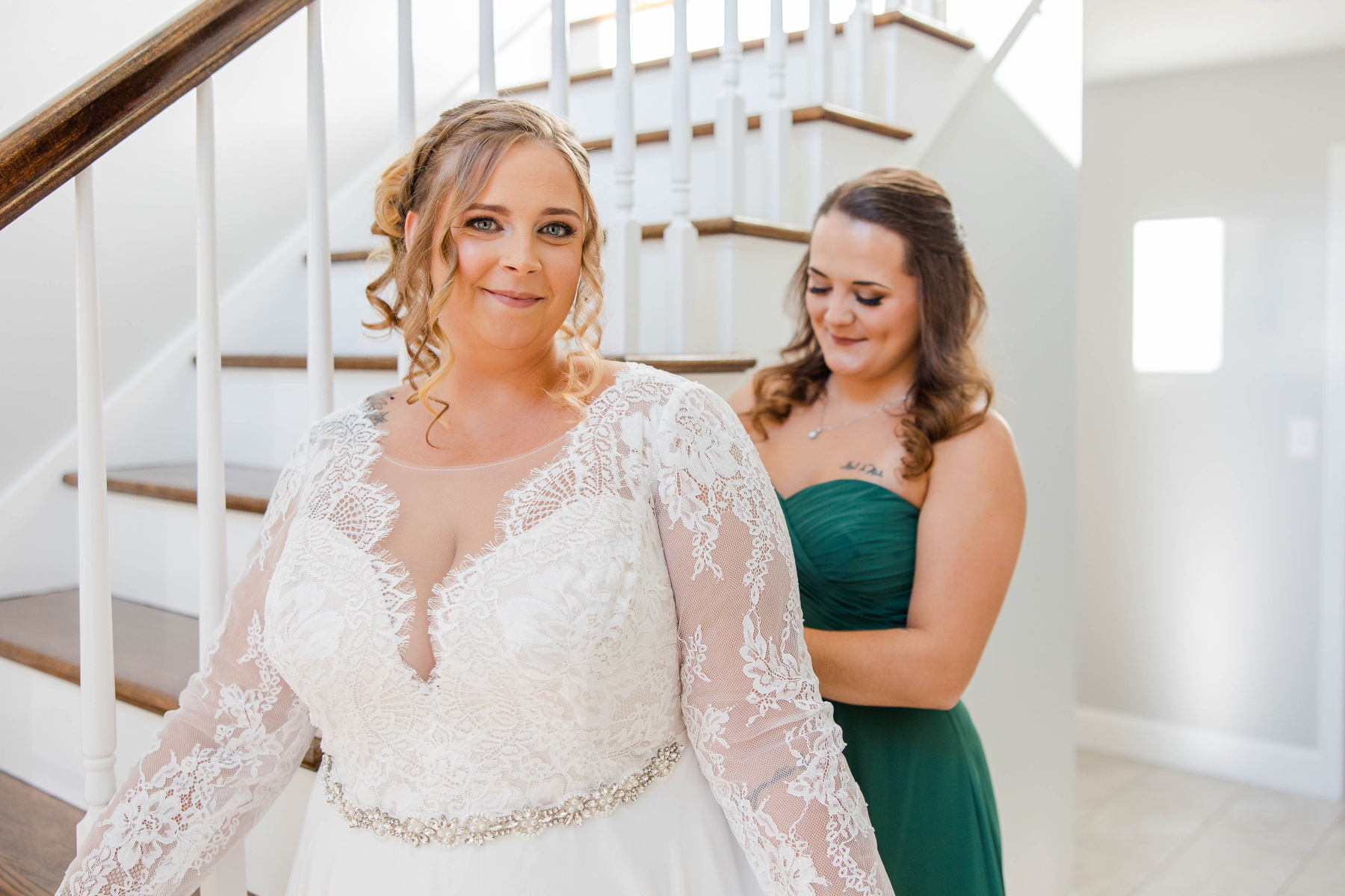 Bride smiles at camera while her maid of honor helps button her dress at Great Neck Country Club Wedding