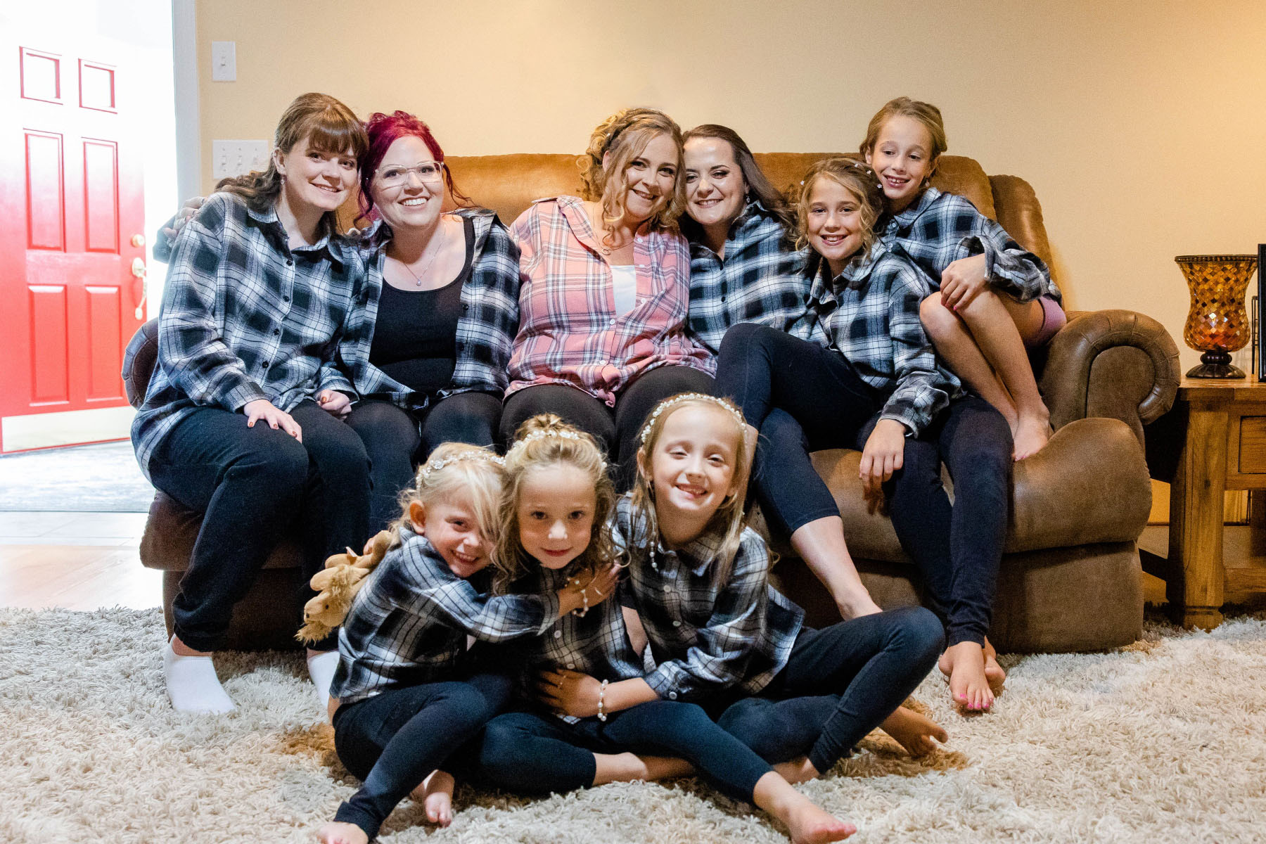 Bride and bridesmaids sit on couch smiling at the camera while wearing flannels at Great Neck Country Club Wedding