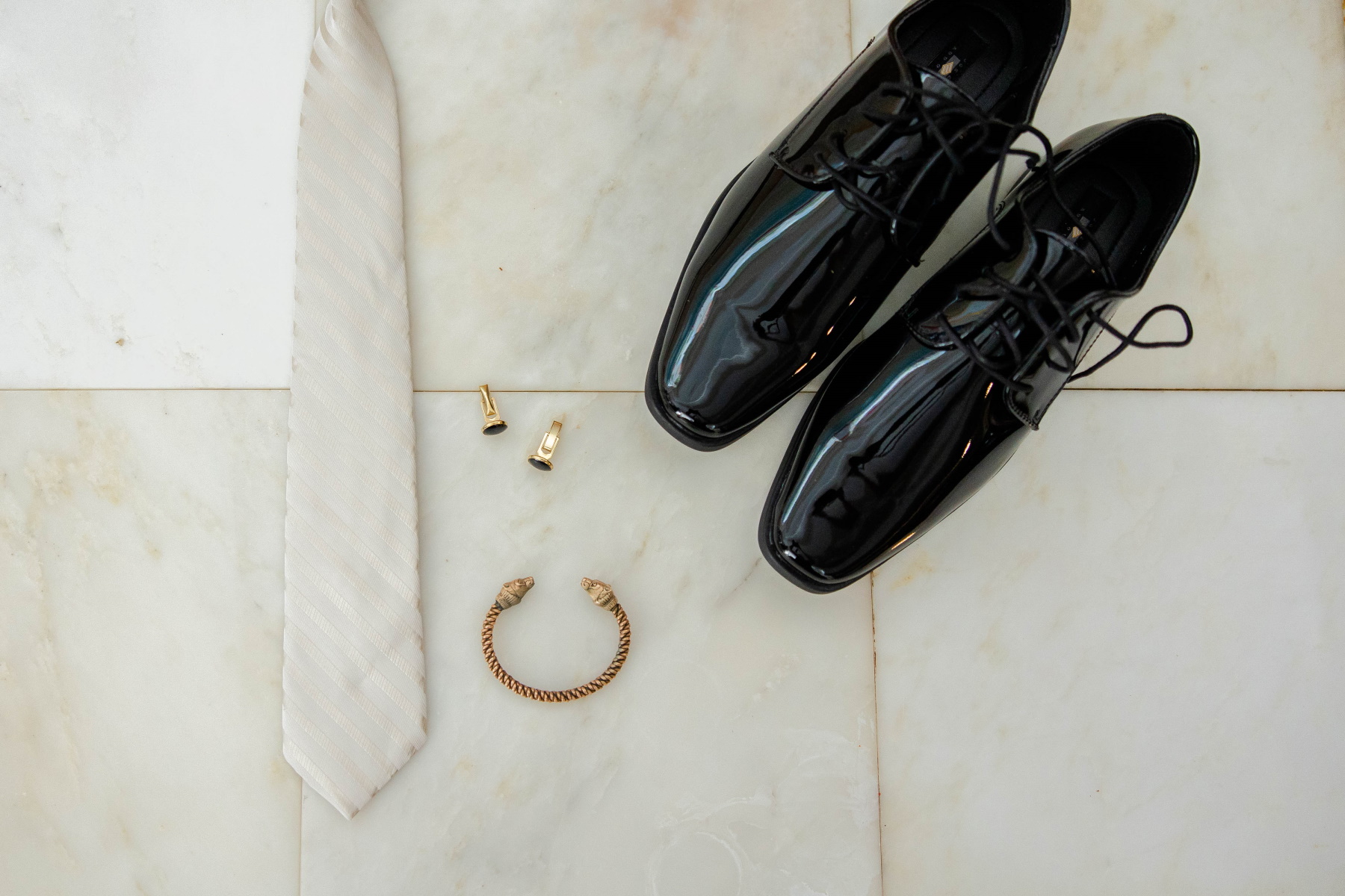 Groom's shoes, cufflinks, bracelet, and ivory sit on slab of marble tile at Great Neck Country Club Wedding