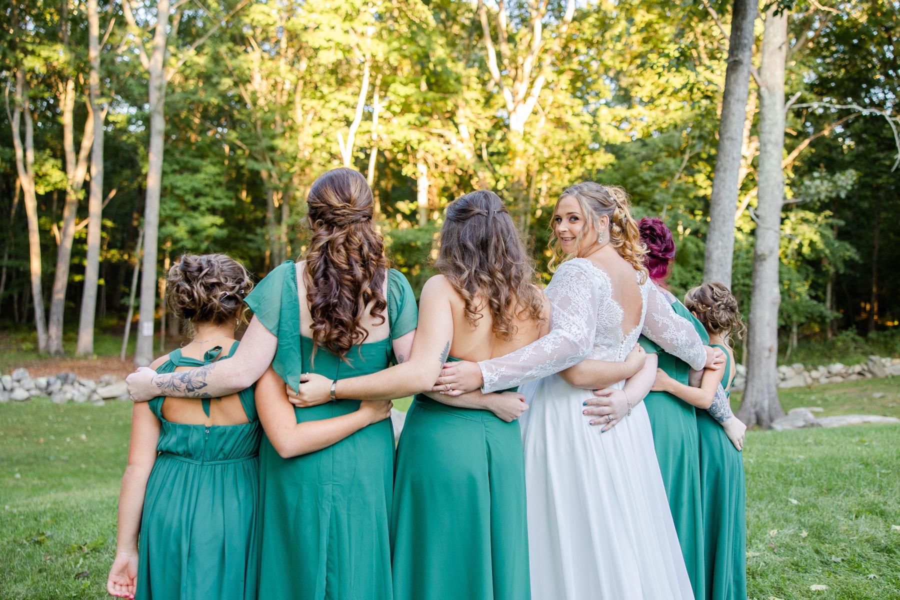 Bride peeks over her shoulder while standing with arms around her bridesmaids at Great Neck Country Club Wedding