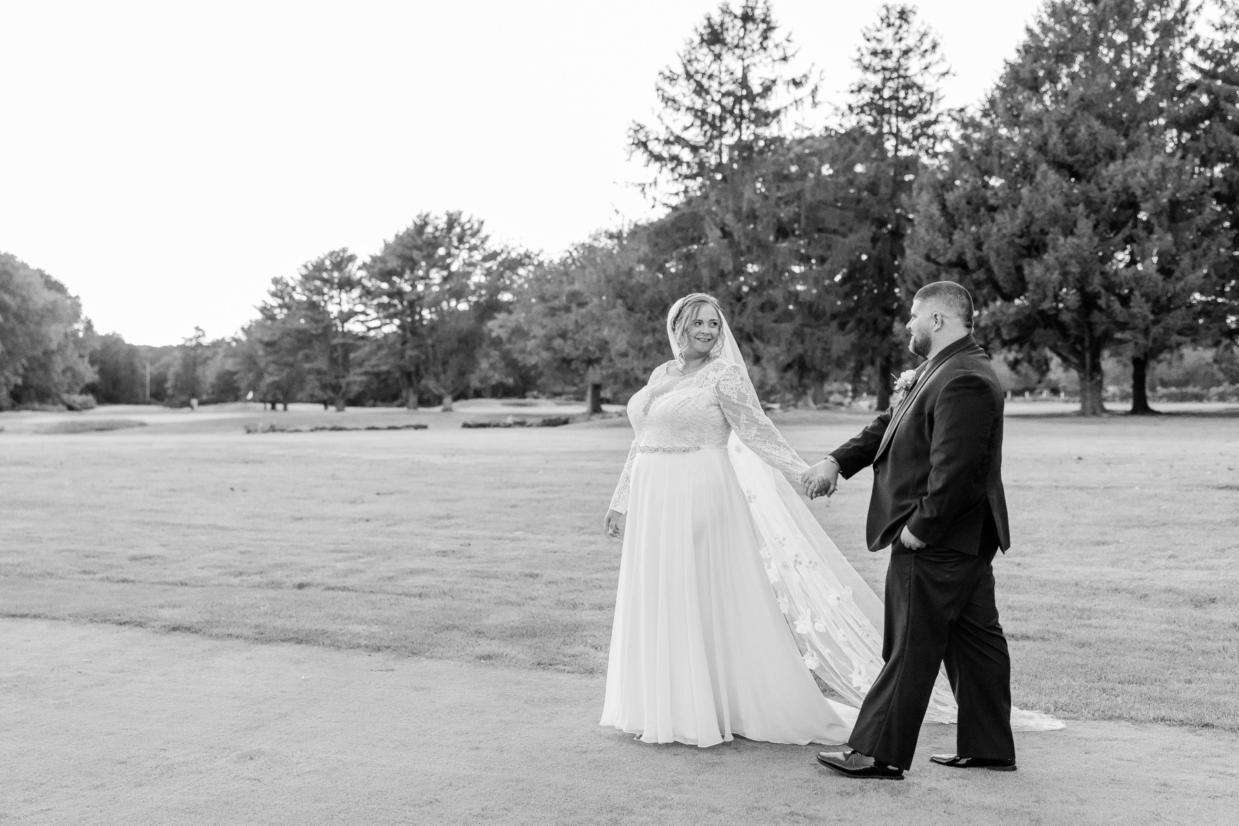 Bride and groom walk while holding hands with a sunset in the background at Great Neck Country Club Wedding