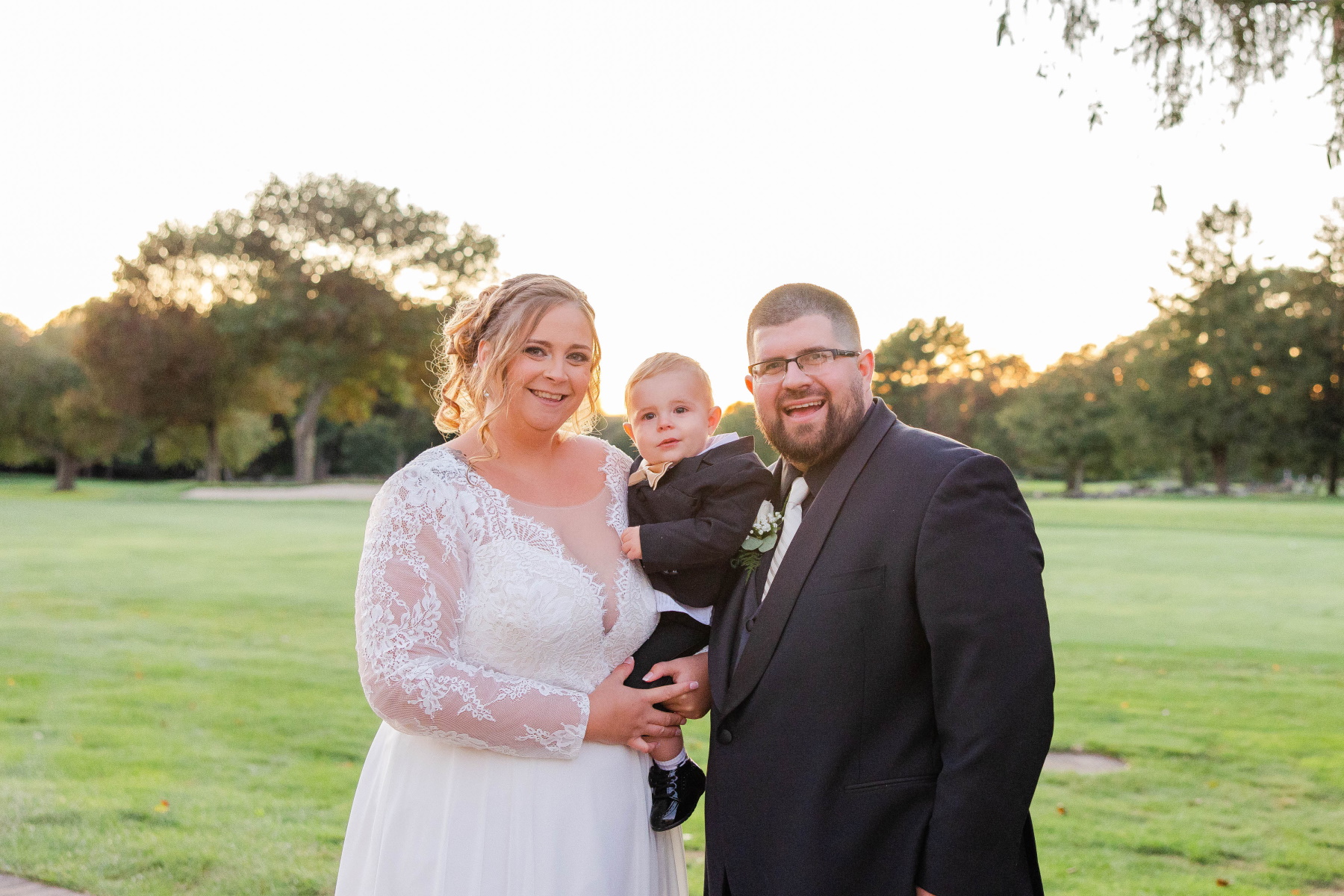 Bride and groom smile at camera while holding their son at Great Neck Country Club Wedding