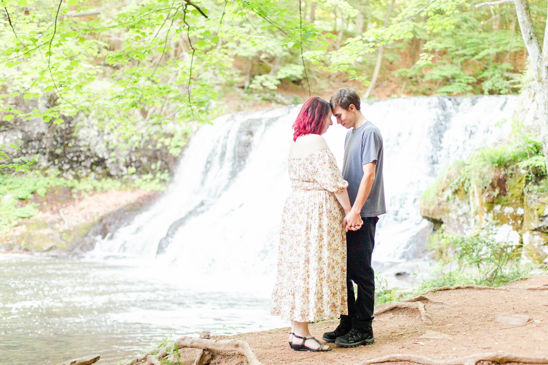 Couple stands with heads together while holding hands next to the waterfall at Wadsworth Fall Engagement Session