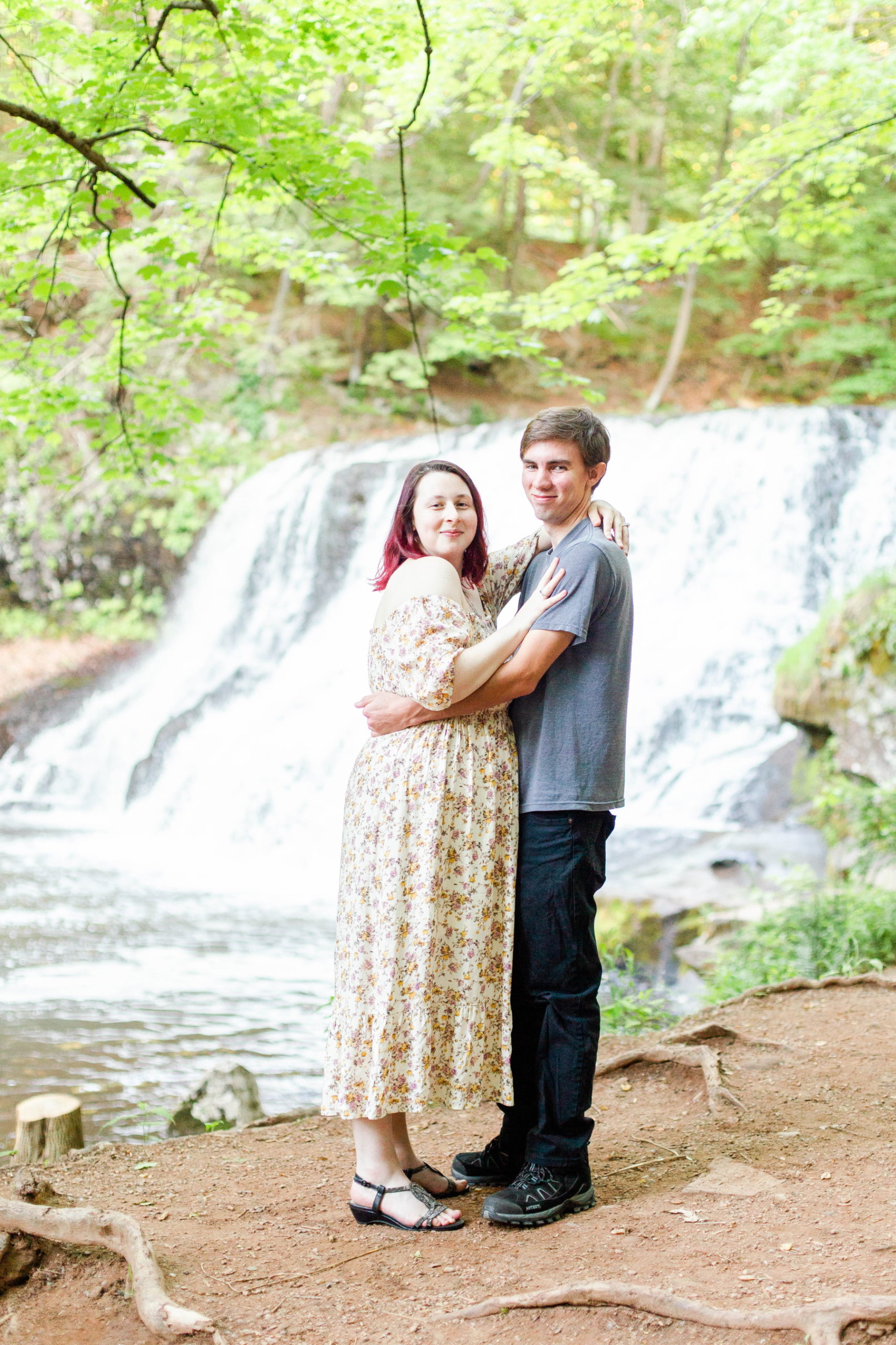 Couples smiles at camera with arms around each other next to waterfall at Wadsworth Fall Engagement Session